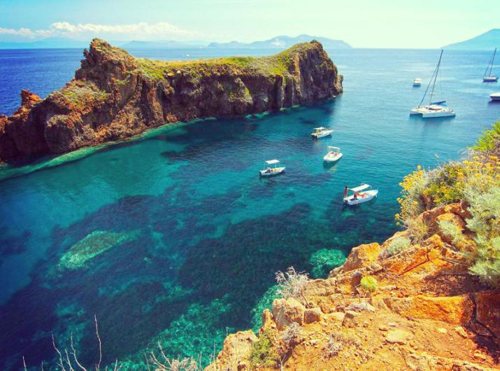 Crystal-clear waters and boats near a picturesque cliff.