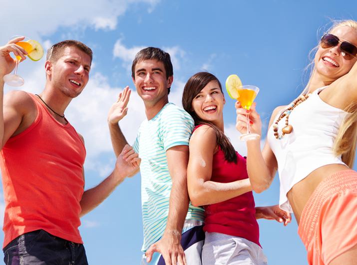 Young people celebrate with cocktails and smiles under a blue sky.