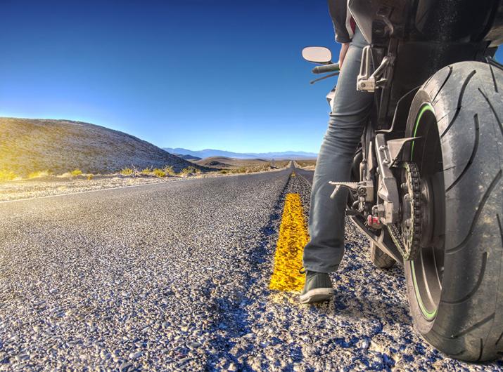 Motorcyclist on a deserted road under a clear, sunny sky.