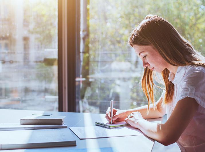 Woman writing in sunlight in a bright room.