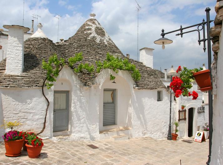 Trullo blanc avec toit conique et fleurs colorées.