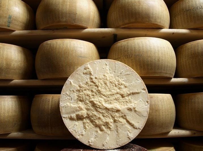 Aged Parmigiano Reggiano wheels on wooden shelves.