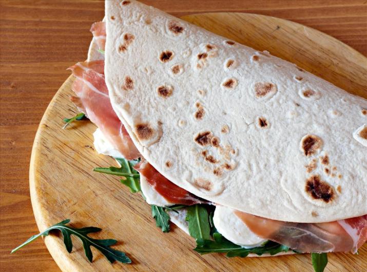 Flatbread with ham, arugula, and mozzarella on wooden board.